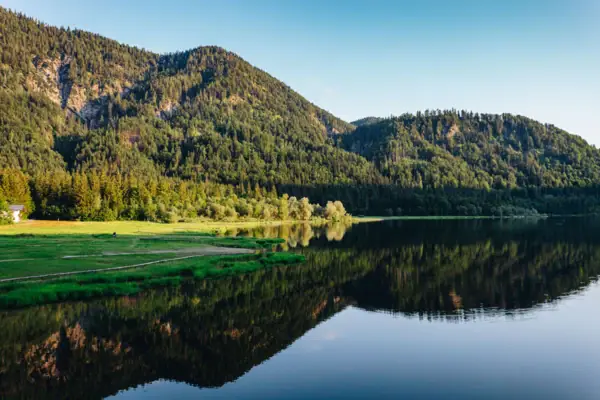 Ein See mit Bäumen und Bergen im Hintergrund.