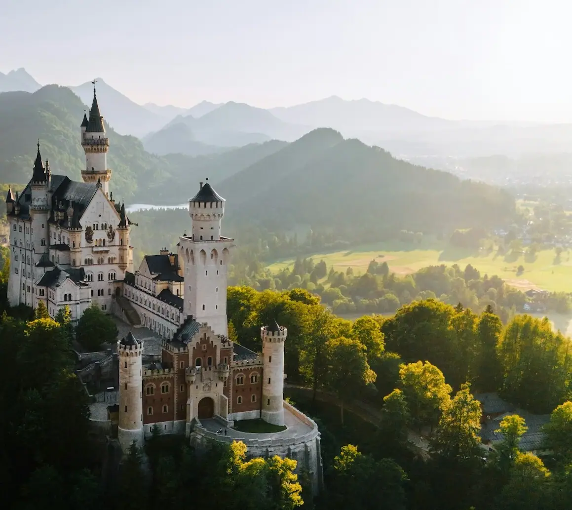 Das Schloss Neuschwanstein auf einem Hügel mit Bäumen und Bergen im Hintergrund.