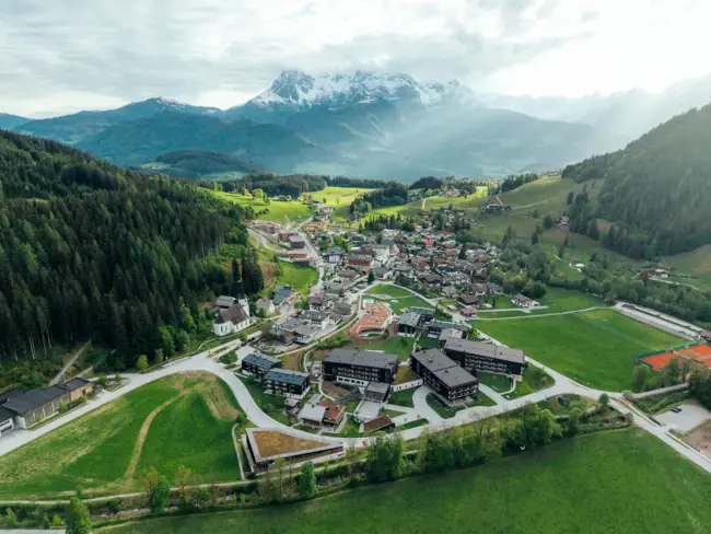 aja Bergresort Werfenweng Bergdorf mit Häusern inmitten von Bäumen und umgeben von Bergen.