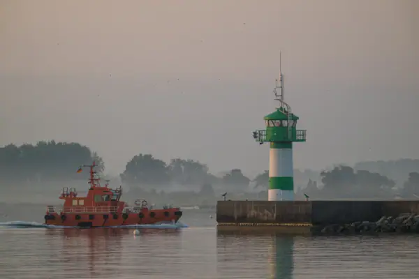 Molenfeuer Travemünde Ein Boot auf dem Wasser mit einem Leuchtturm im Hintergrund.