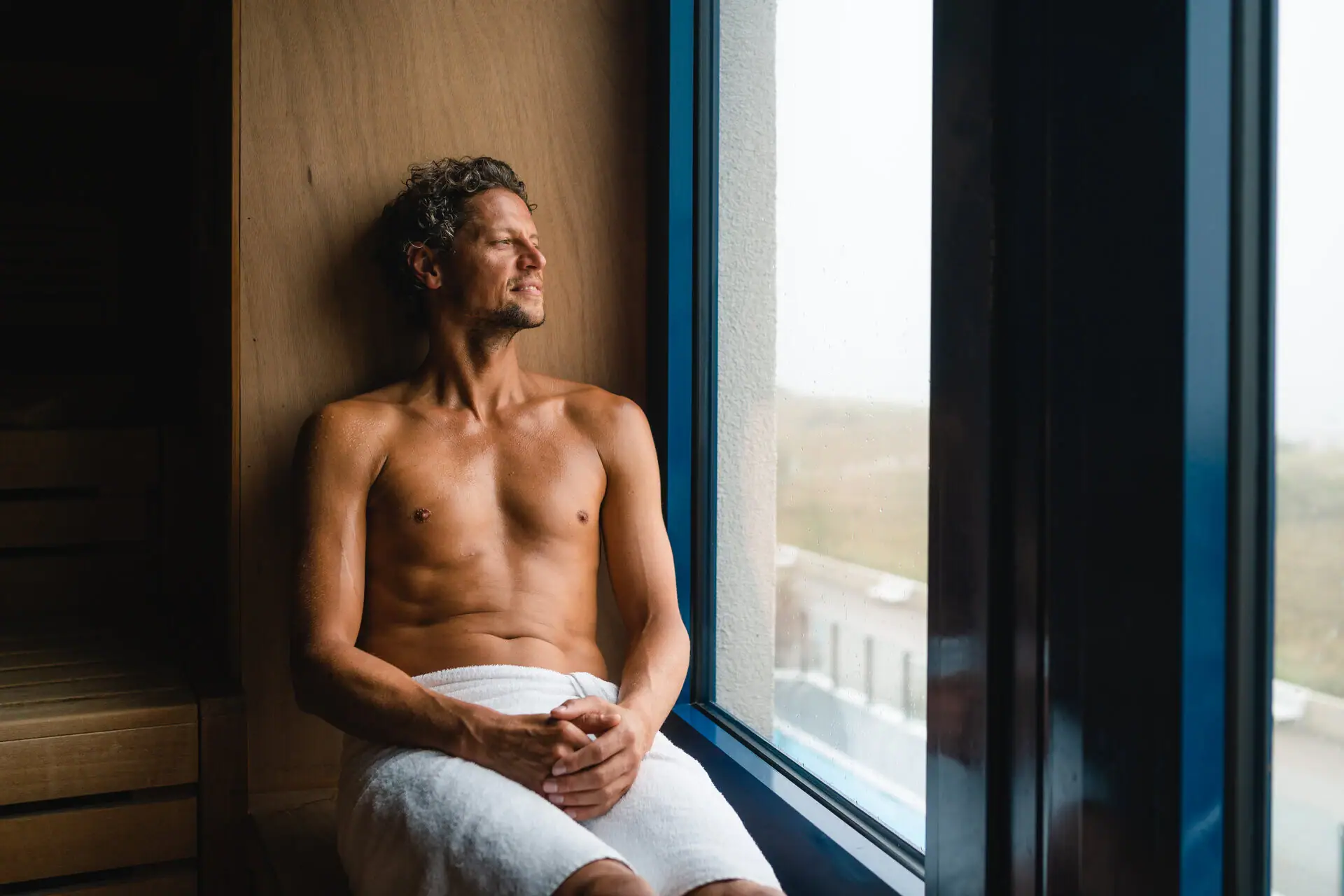 Sauna im aja Warnemünde Ein Mann sitzt auf einer Saunabank und schaut raus aus dem Fenster.