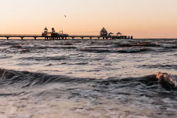 Seebrücke Ein Gewässer mit einem Pier und einem Gebäude in der Ferne.