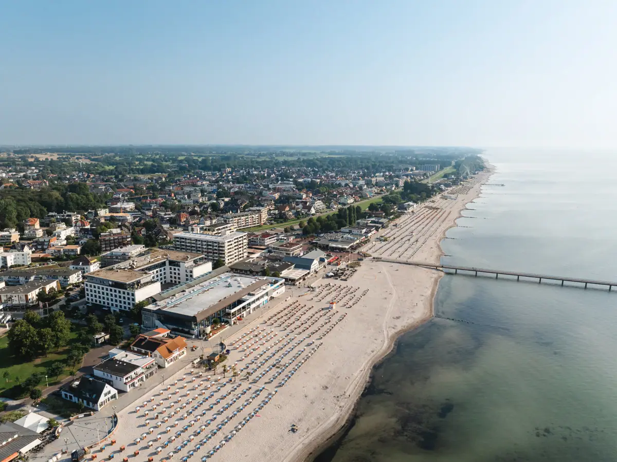 Grömitz Luftaufnahme eines Strandes mit Gebäuden und einem Gewässer im Hintergrund.