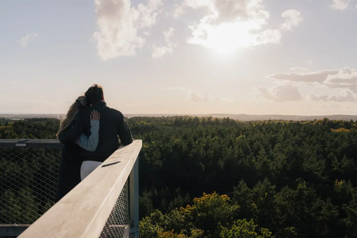 Ein Mann und eine Frau umarmen sich auf einem Balkon mit Blick auf dem Baumwipfelpfad