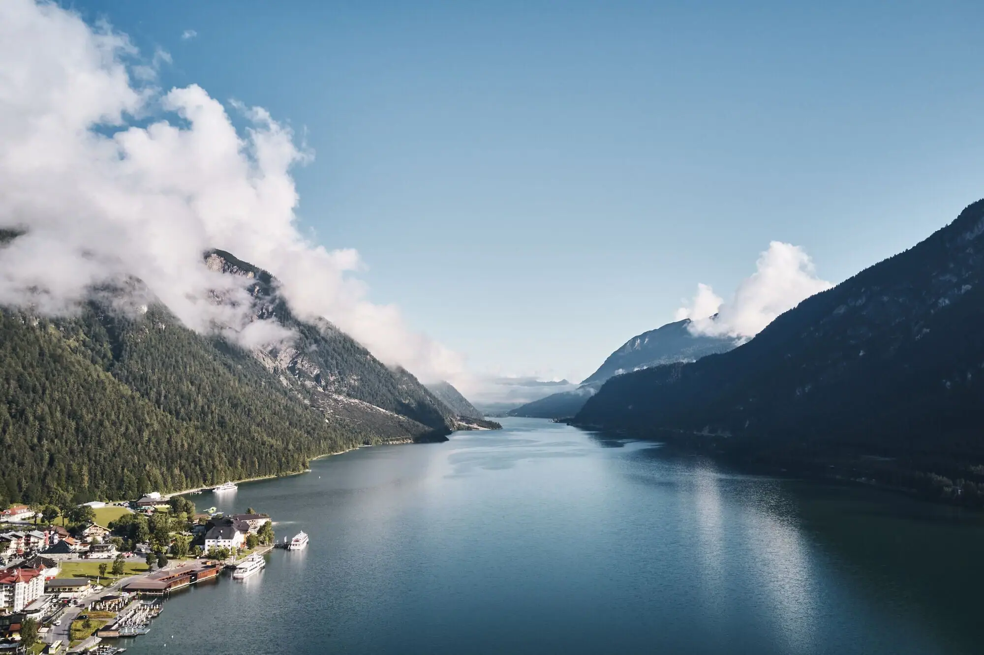 Achensee Ein Gewässer mit einem Haus und Bergen im Hintergrund.