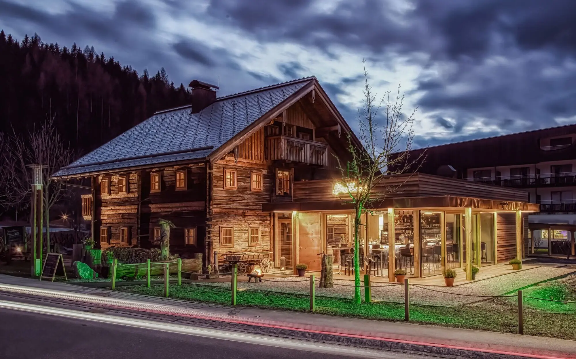 An old wooden house with a conservatory and a tree in front of it.