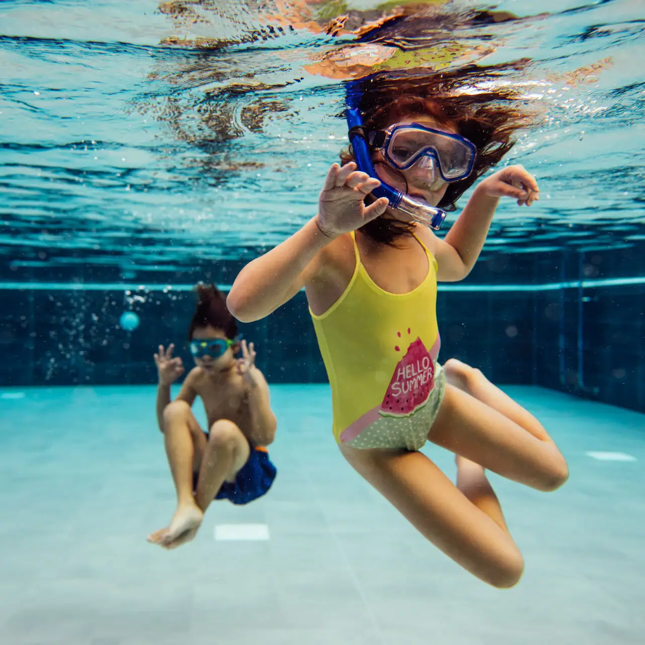 Zwei Kinder schwimmen unter Wasser in einem Schwimmbad.