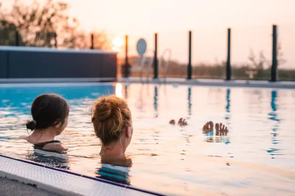 Zwei Frauen schwimmen in einem Außenpool bei Sonnenuntergang.