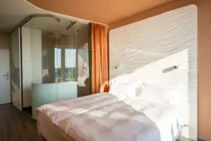 Zimmer im aja Warnemünde Ein Bett vor einer Glaswand in einem stilvollen Schlafzimmer.