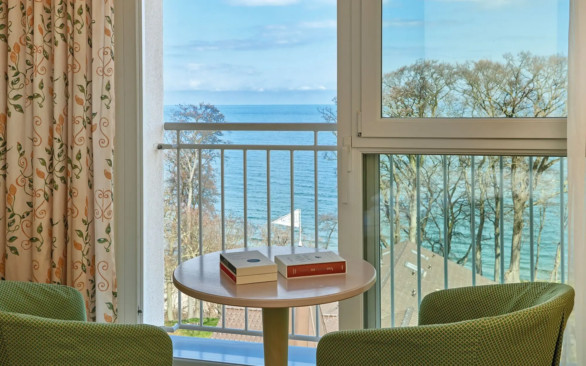 Ein Tisch mit Büchern darauf, neben einem Balkon mit Blick auf das Meer.