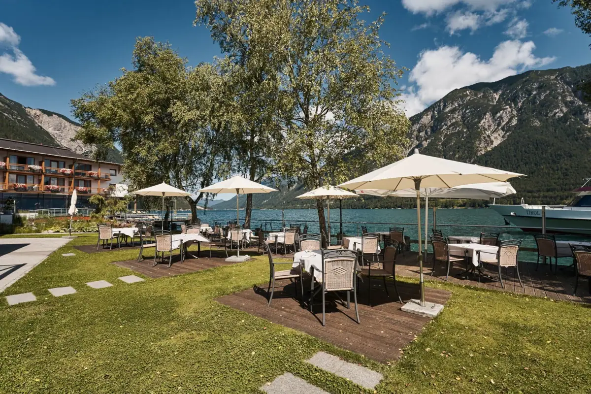 Seeterrasse Eine Gruppe von Tischen und Sonnenschirmen auf einer Wiese am See.
