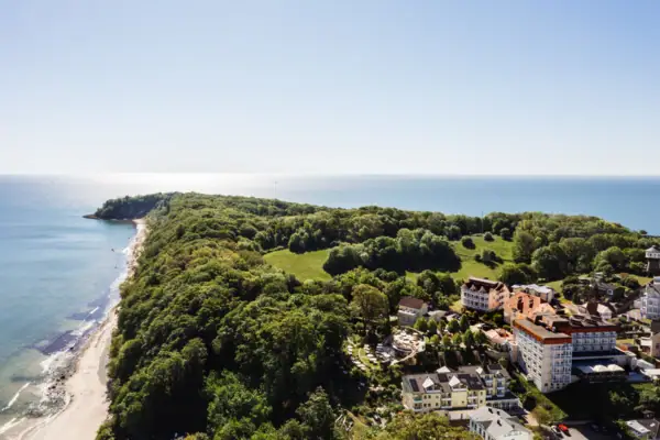 Landschaft mit Bäumen und Gebäuden, im Hintergrund Küstenlinie und Meer.