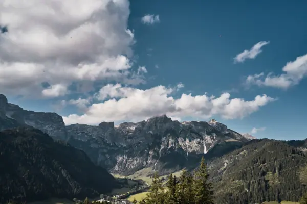Bergkette mit Bäumen und Wolken im Vordergrund.
