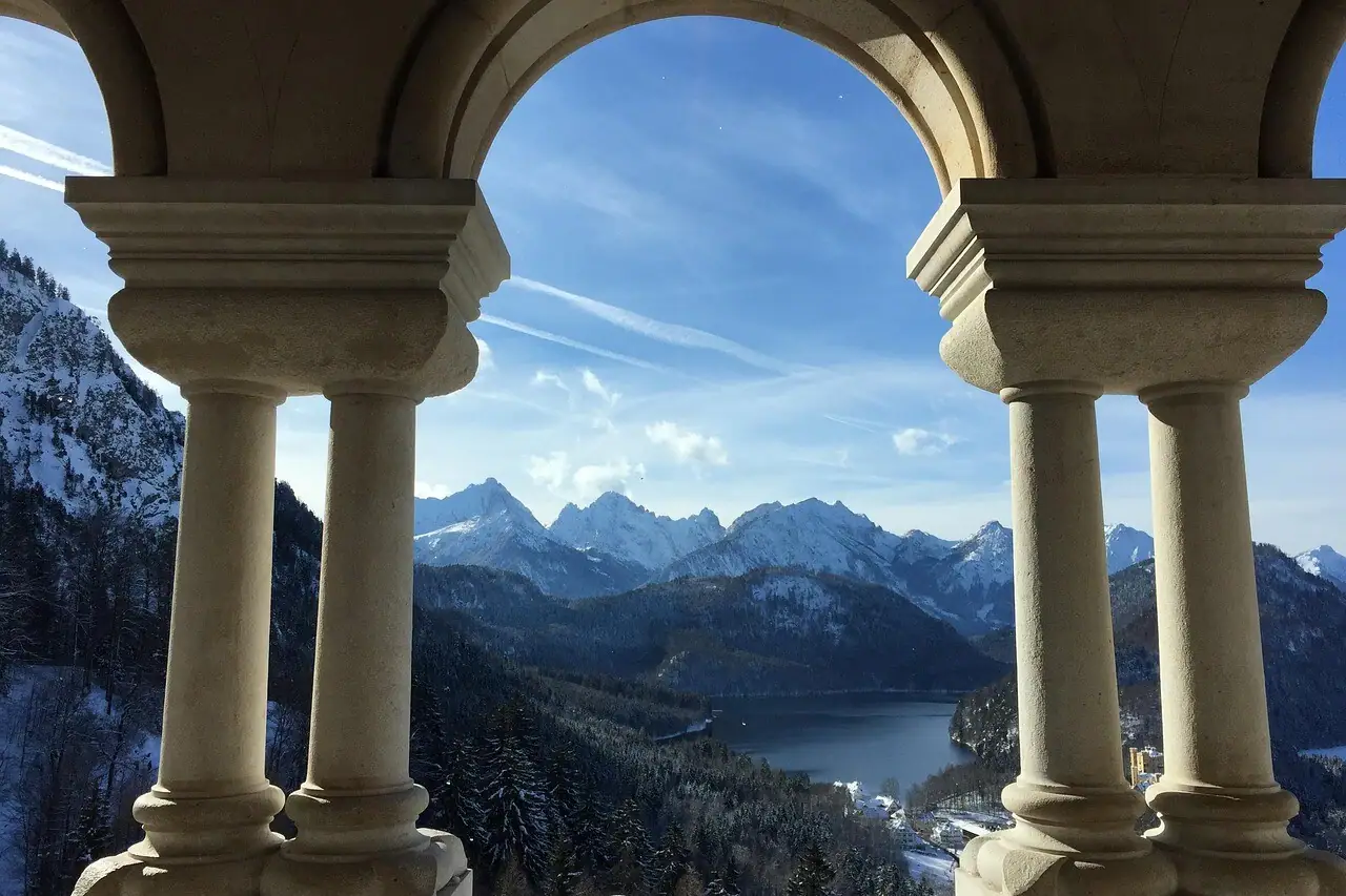 Ausblick vom Schloss Neuschwanstein durch einen Steinbogen mit Blick auf Berge und einen See.