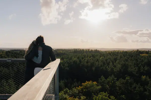 Ein Mann und eine Frau umarmen sich auf einem Balkon mit Blick auf dem Baumwipfelpfad Usedom.