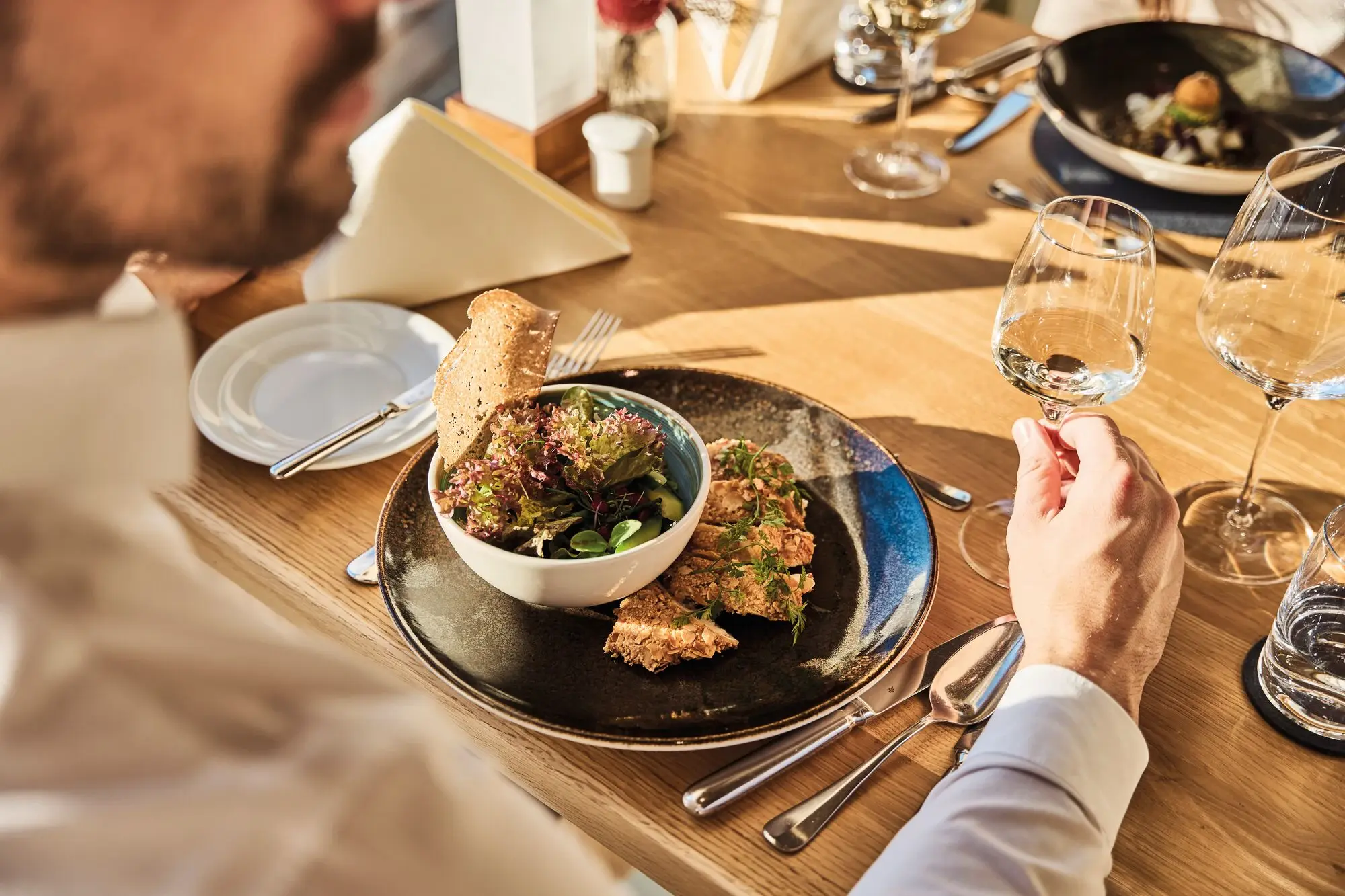 Man eats salad and drinks a glass of wine at the table.