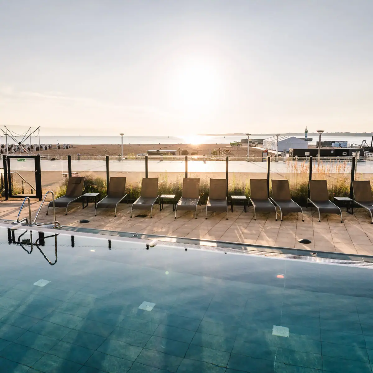 Ein Pool mit Stühlen und einem Strand im Hintergrund.