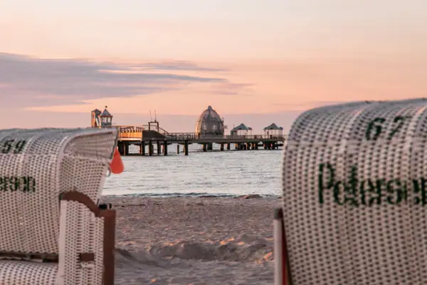 Ein Strandkorb am Strand mit einem Pier im Hintergrund.