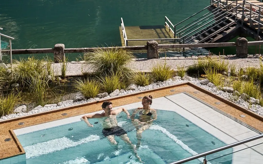 Menschen im Außen-Whirlpool mit einem See und Bergen im Hintergrund.