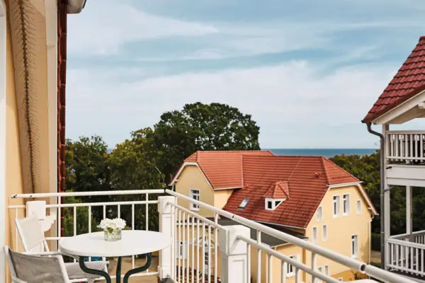 Ein Balkon mit Tisch, einem Haus und Bäumen im Hintergrund.