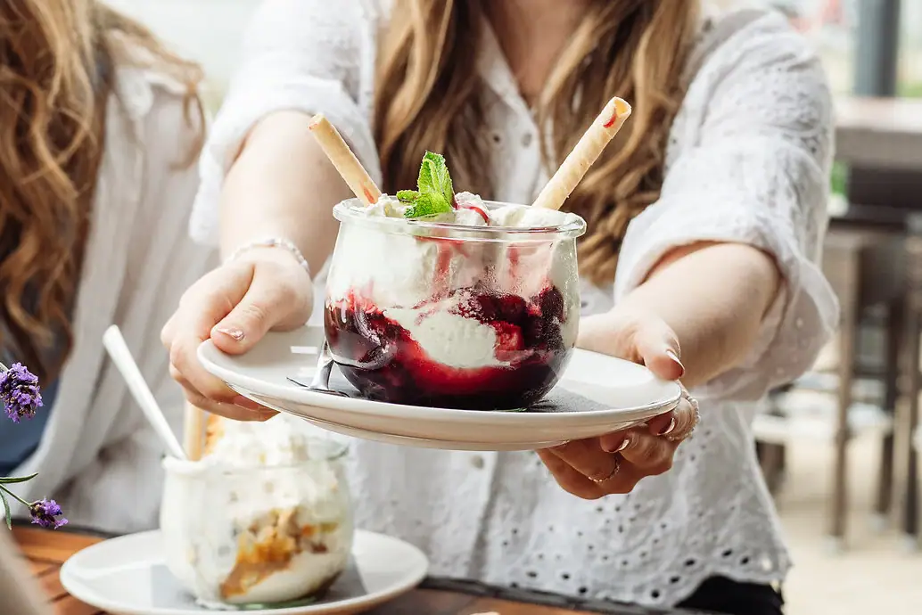 Eis im aja Warnemünde Eine Frau hält einen Teller mit einem Eisbecher mit Vanilleeis und Kirschen..