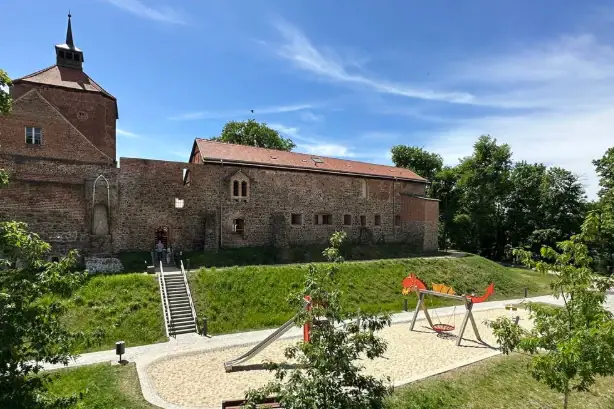 Ein Spielplatz vor einem Gebäude mit Bäumen und blauem Himmel.