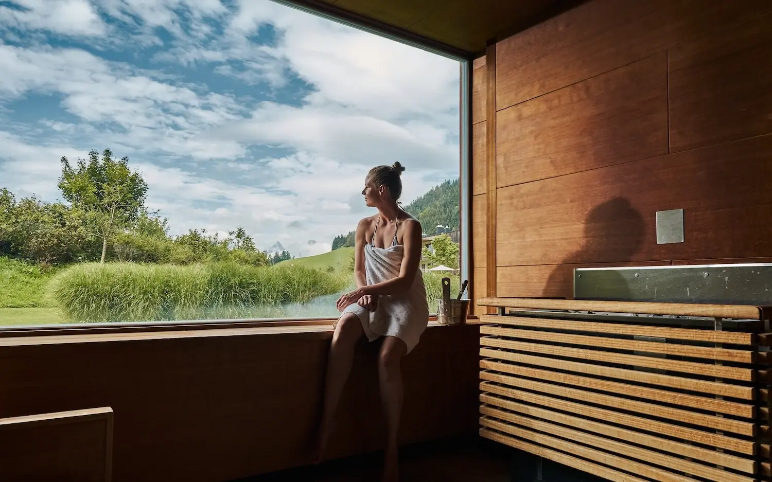 Woman sits in a sauna on a windowsill and looks outside.