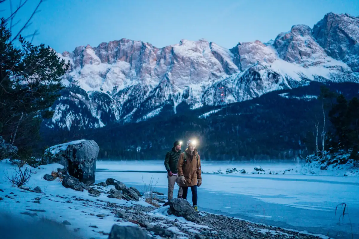 Winterwanderung Ein Paar steht mit Stirnlampe an einem felsigen Ufer.