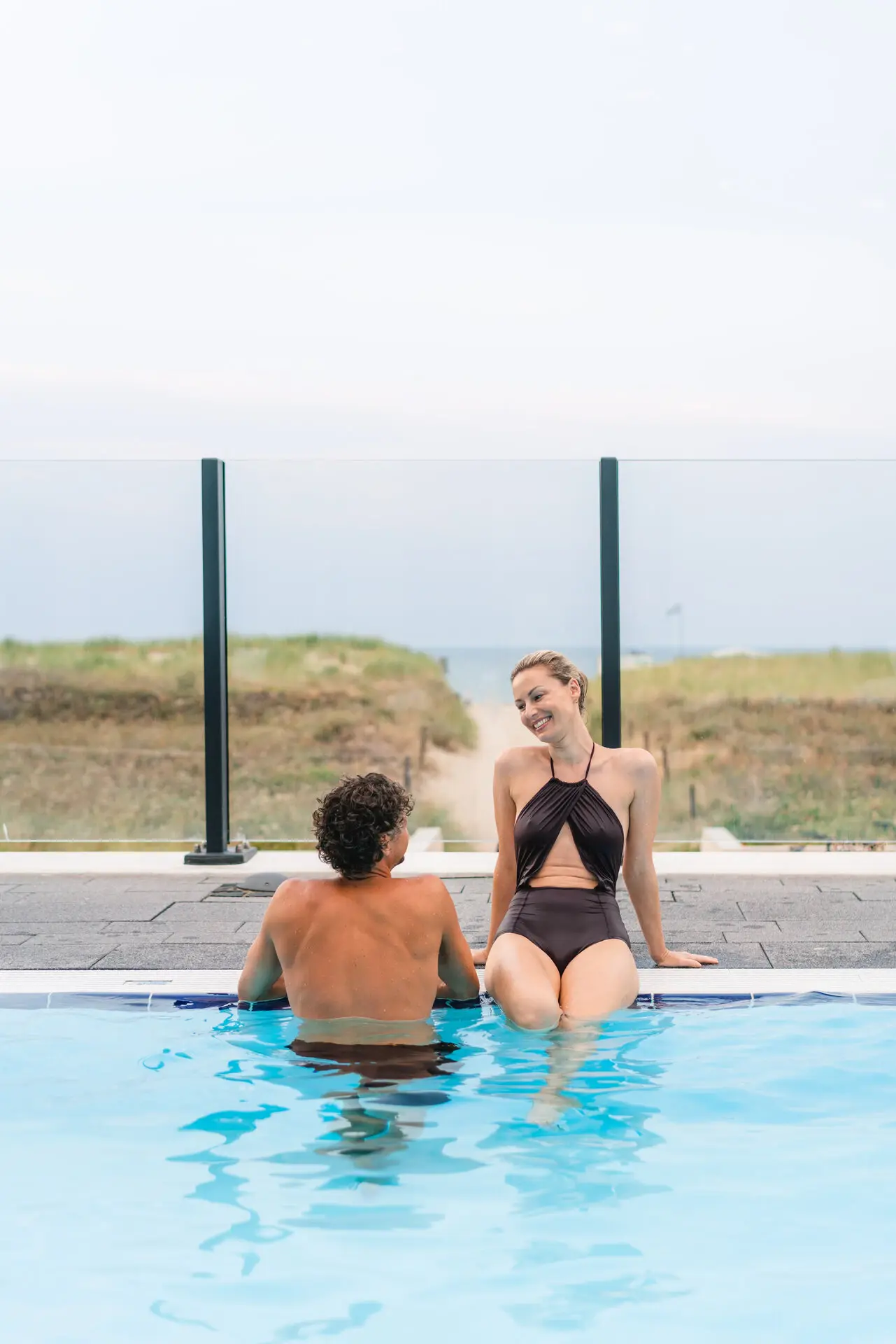 A man and woman sitting in a swimming pool, both wearing swimwear.