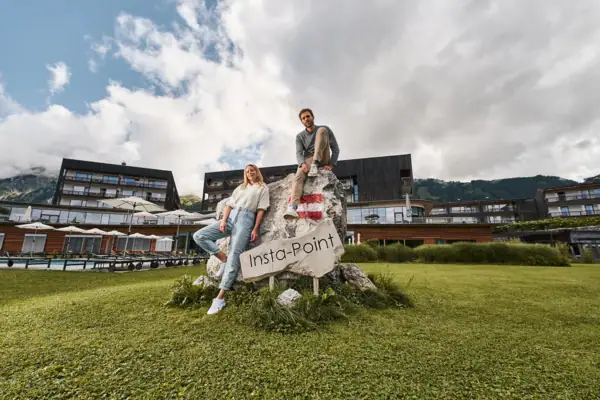 Ein Mann und eine Frau sitzen auf einem Felsen mit einem Schild, im Hintergrund das Hotelgebäude.