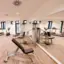 Ansicht eines Fitnessraums mit mehreren grauen Geräten und Spiegelwand.
