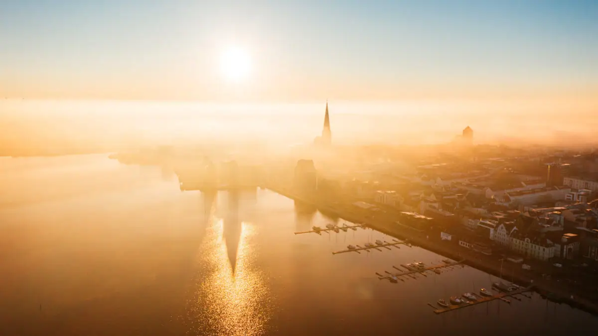 Rostock im Nebel Eine Stadt im Nebel mit Wasser im Vordergrund.
