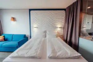 Ein Bett mit weißen Laken und ein blauer Couch.