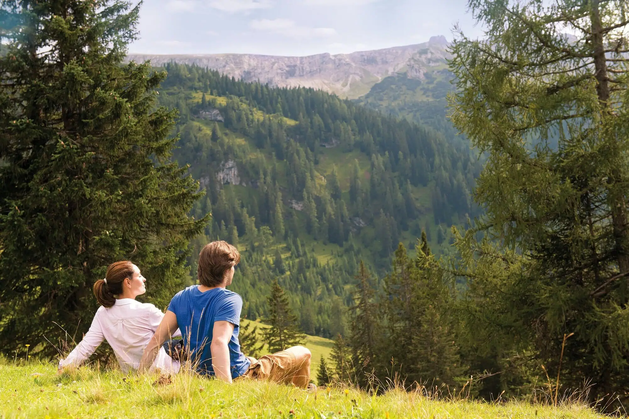 Paar macht Rast Ein Mann und eine Frau sitzen auf einem Hügel und blicken auf einen Berg.
