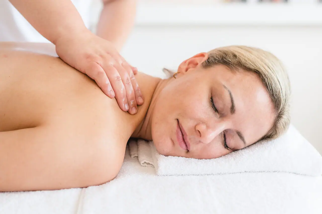 Massage Eine Frau liegt mit geschlossenen Augen auf einem weißen Handtuch.