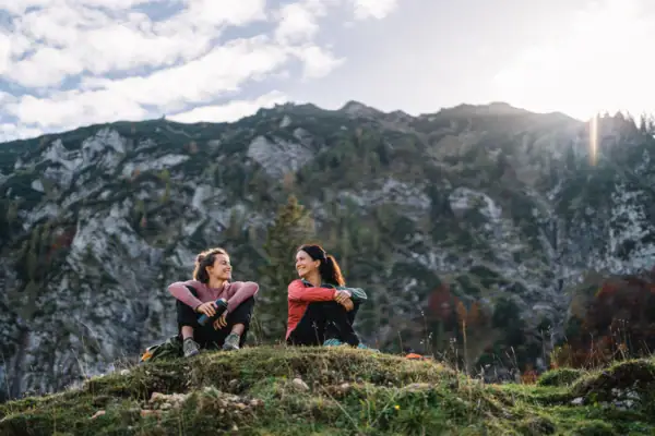 Wandern in Ruhpolding Zwei Frauen sitzen auf einem Hügel mit Bergen im Hintergrund.