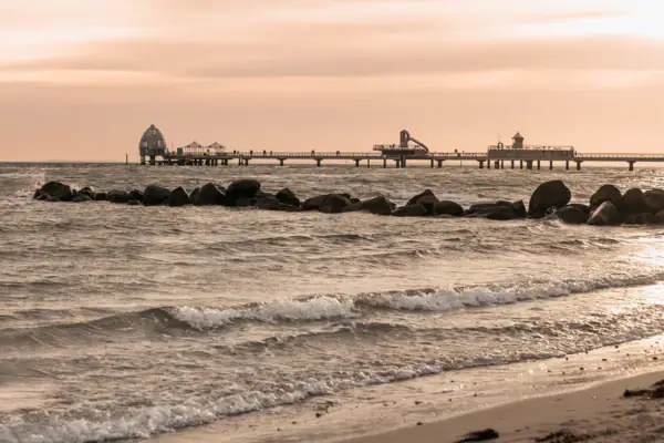 Strand mit einem Pier und Felsen bei Sonnenuntergang.