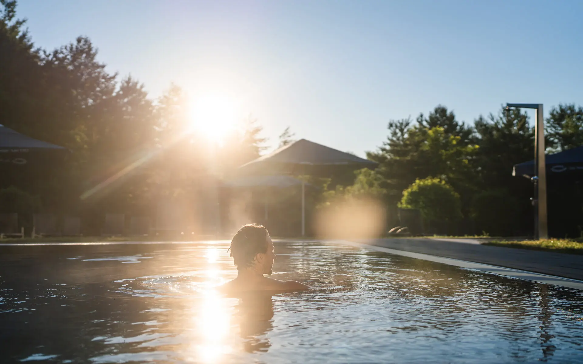 Ein Mann schwimmt bei Sonnenaufgang im Außenpool des aja bad Saarow.