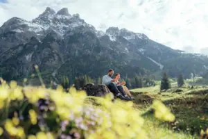 Ein Mann und eine Frau sitzen auf einem Felsen vor einem Berg.
