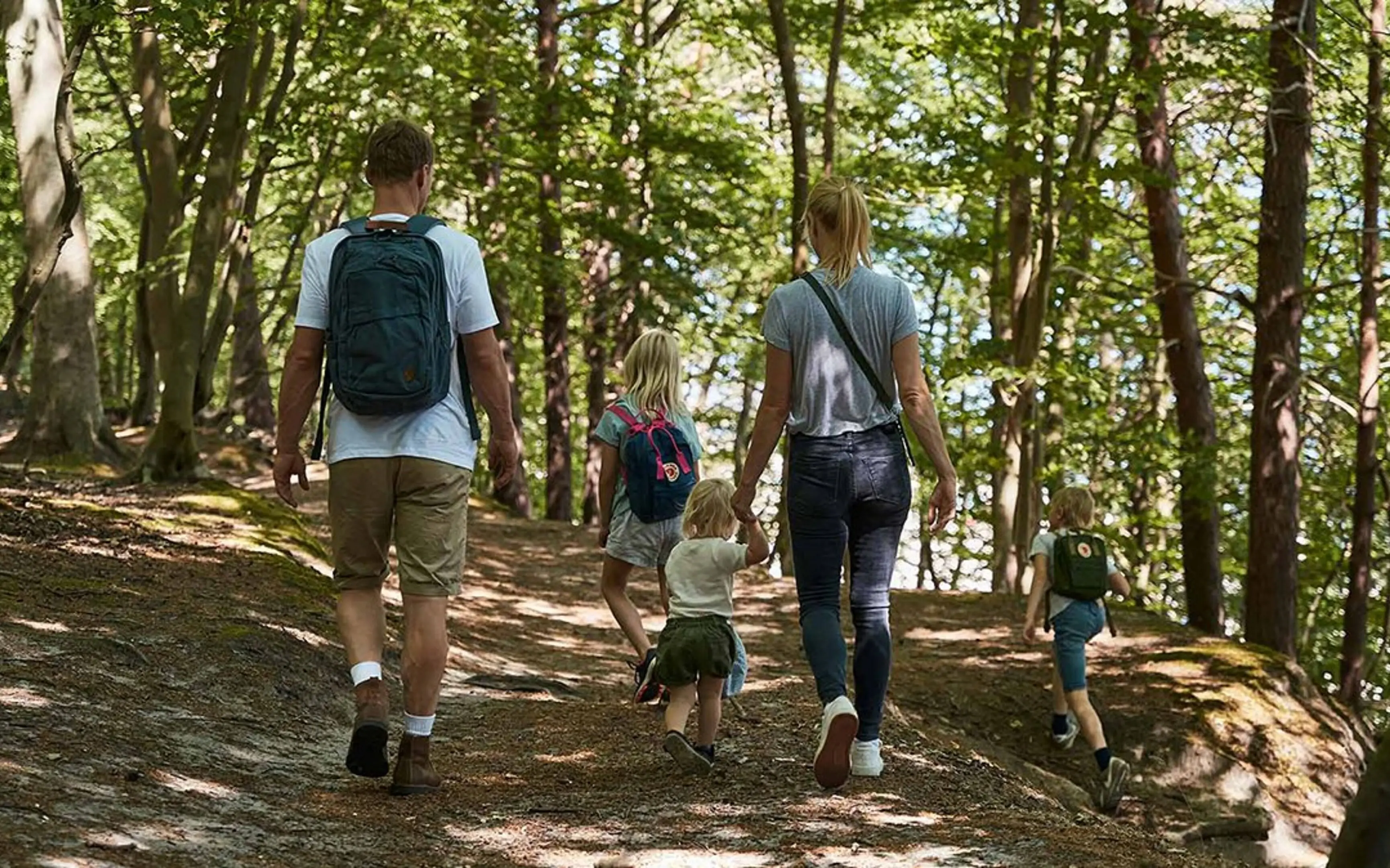 Eine Familie mit 3 Kindern, die auf einem Waldweg gehen.