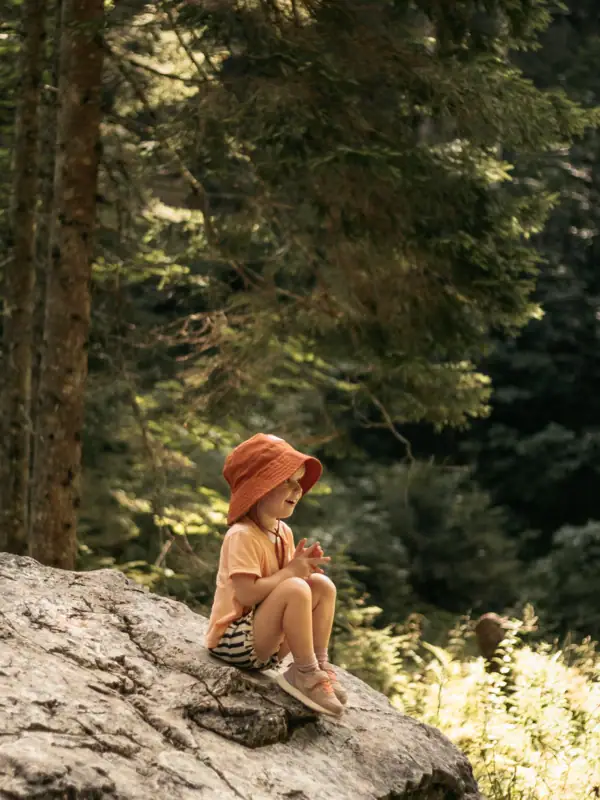 Ein Kind sitzt auf einem Felsen im Wald.