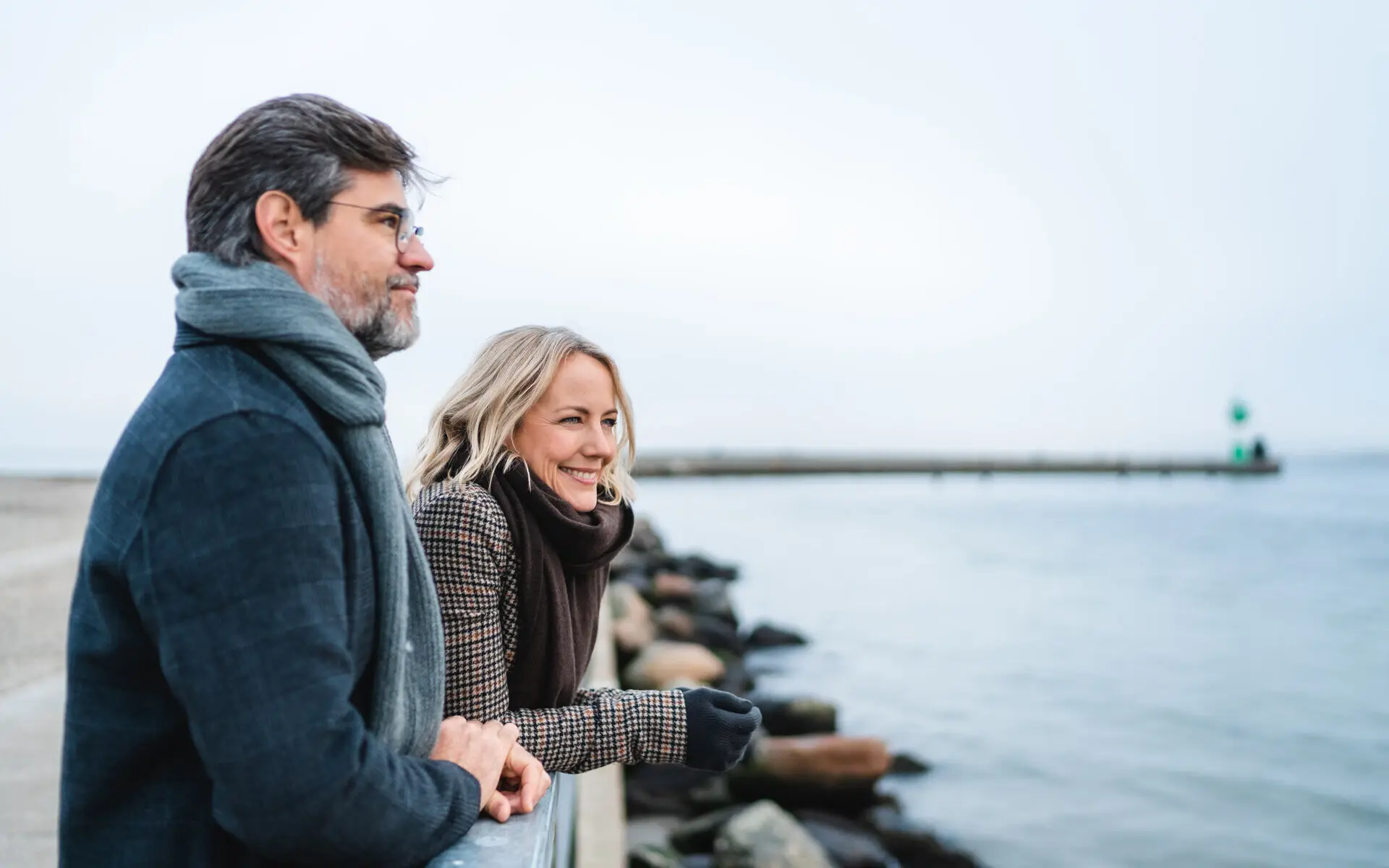 Ein Mann und eine Frau lehnen an einem Geländer und blicken auf das Wasser.