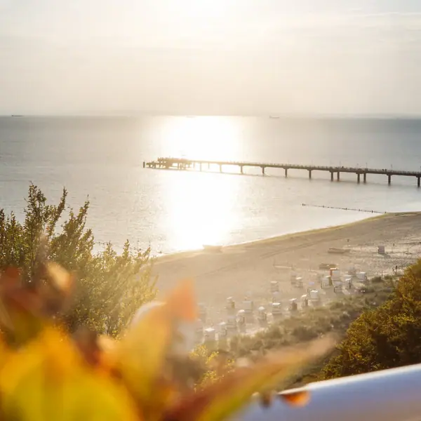 Ausblick Ein Pier an einem Strand unter freiem Himmel mit Wolken und Wasser im Hintergrund.