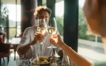 Zwei Menschen sitzen an einem Tisch im Restaurant und stoßen mit einem Glas Wein an.