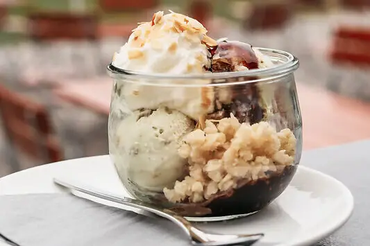 Eine Glasschale mit Eiscreme und Toppings auf der Terrasse von der aja Bar Ruhpolding..