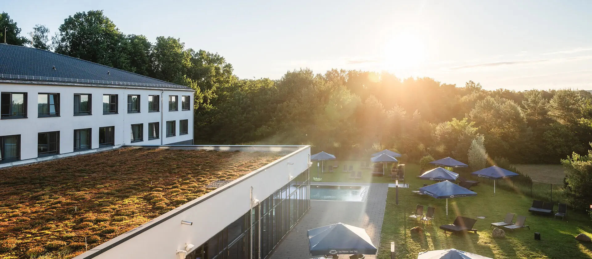 Das aja Hotel Bad Saarow mit Sonnenschirmen, Gras und Stühlen sowie einem Außenpool.