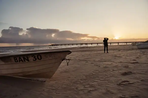 Eine Person steht am Strand neben einem Boot.