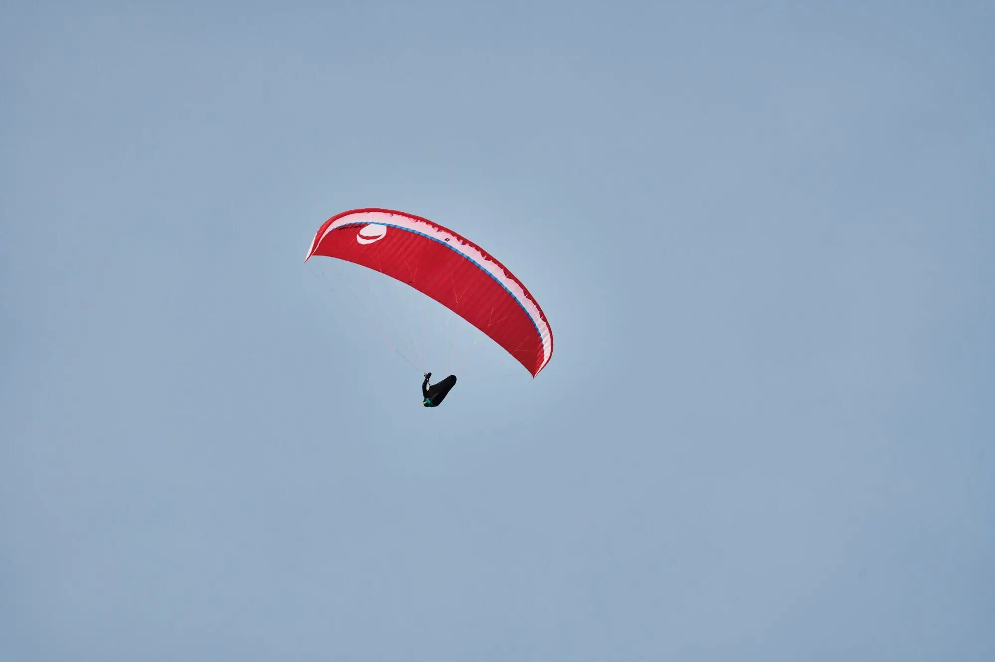 Paragleiten in Werfenweng Person beim Paragliden schwebt mit einem roten Schirm vor dem bleuen Himmel.