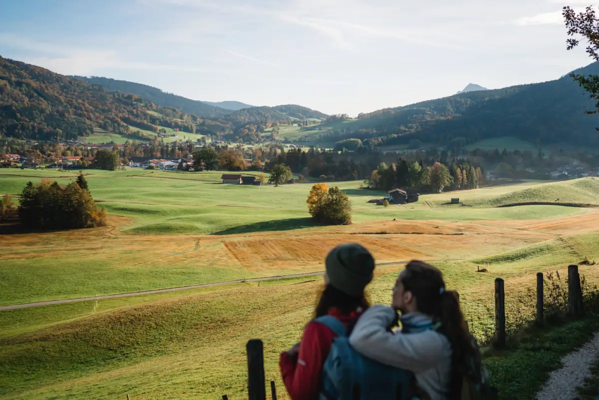 Zwei Personen betrachten eine Landschaft mit Bäumen und Wolken am Himmel.