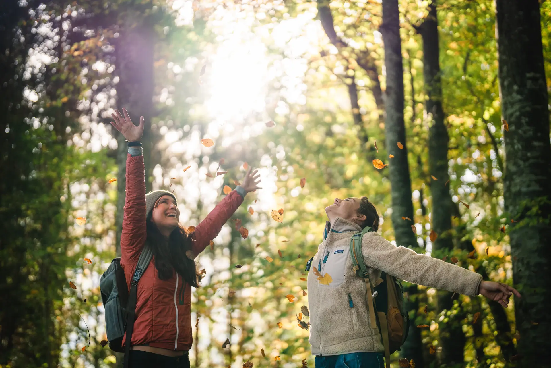 Zwei Personen werfen im Herbstwald Blätter in die Luft.